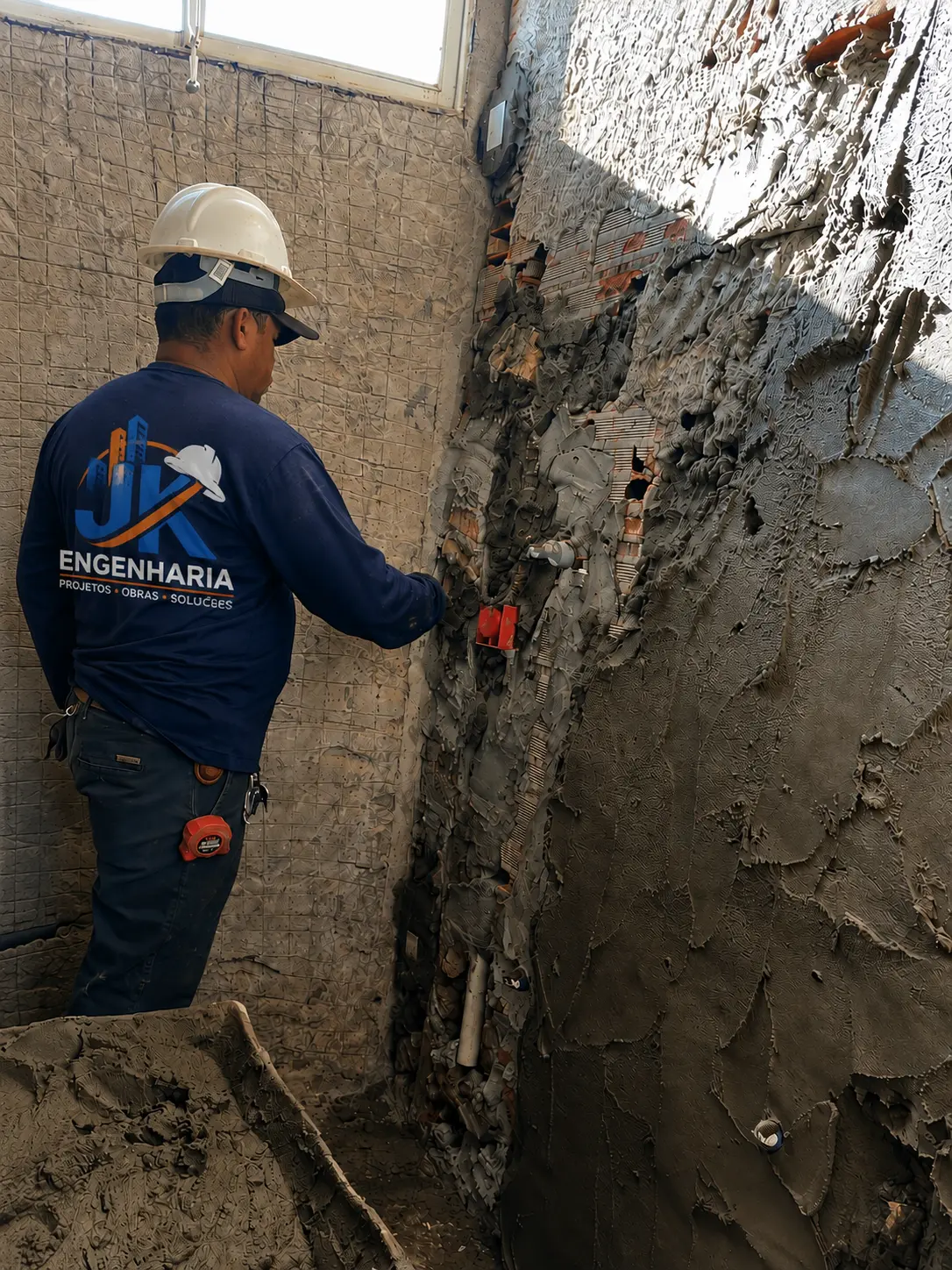 Profissional da equipe JK Engenharia executando reboco e embutimento de tubulação em parede de alvenaria